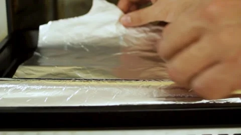 Chef's hands place a roll of foil on a baking tray. The foil roll is unfolded Stock Footage 304877262