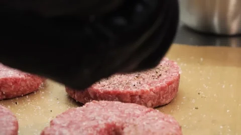 Chef's hands seasoning raw beef burger patties with salt and pepper on a kitchen Stock Footage 331632948