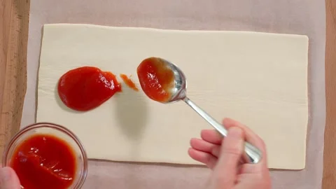 Chef's hands spread tomato sauce on puff pastry with spoon Stock Footage 264141543