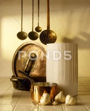 A chef's hat, copper pots, ladles and garlic Stock Photos
