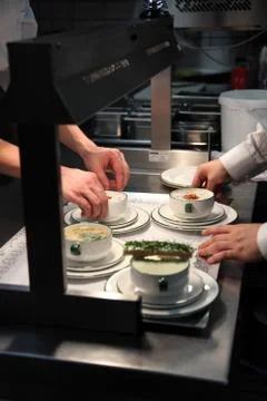 Chefs plating up different hot soups in a restaurant kitchen Stock Photos