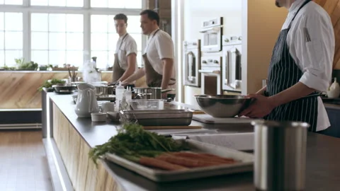 Chefs preparing food around a large countertop full of kitchen tools in interior Stock Footage 199457803