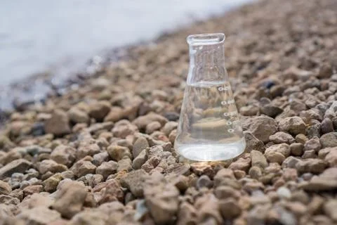 Chemical flask with water, lake or river in the background. Stock Photos