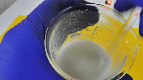 Chemist in blue gloves stirring a white cosmetic liquid emulsion with a glass Stock Footage 334822222