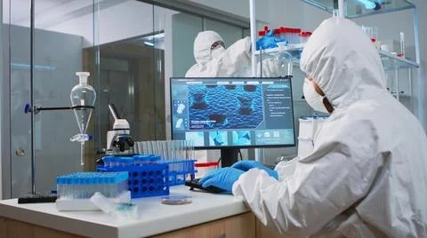 Chemist in coverall typing on computer analysing vaccine evolution Stock Photos
