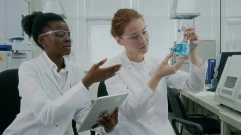 Chemist Examining Liquid Solution while Speaking to Coworker with Tablet Stockbeeldmateriaal 294591842