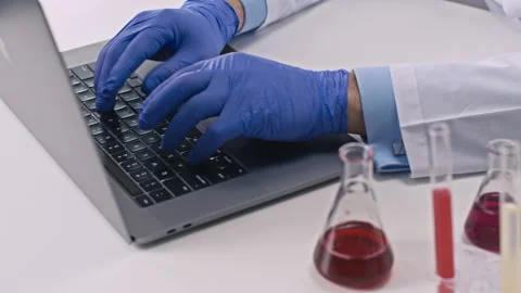 Chemist in gloves in innovation lab typing on laptop. Close-up Stock-Footage 130756415