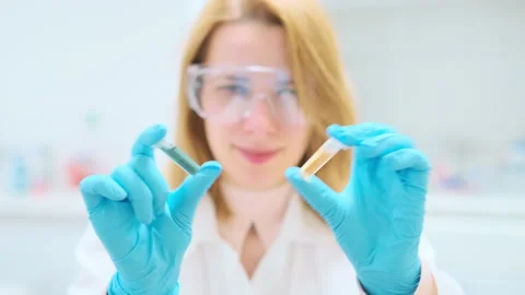 Chemist in goggles shaking test tubes with blue and yellow solution Stockbeeldmateriaal 244467543