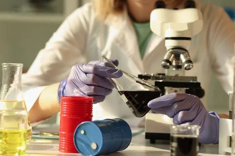 Chemist is holding flask of oil while sitting at research laboratory table. Stock Photos