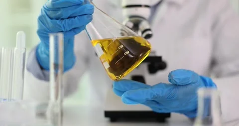 Chemist laboratory technician holds flask with yellow liquid in hands in Video stock 252935038