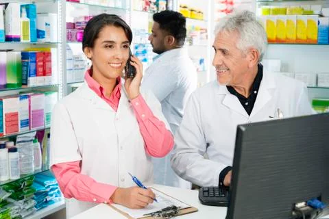 Chemist Looking At Female Colleague Using Telephone At Counter 写真素材