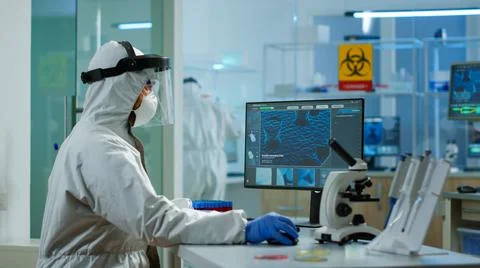 Chemist in ppe suit typing on computer checking vaccine development Stock Photos