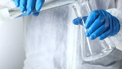 Chemist in protective gloves lab pours solution from beaker into  glass tube. Stockbeeldmateriaal 151456125