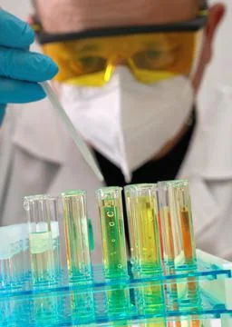 Chemist with protective goggles, mask and gloves, working in lab, dropping .. Stock Photos