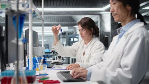 Chemist using laboratory glassware with indicator solution next to coworker Stockbeeldmateriaal 320144707
