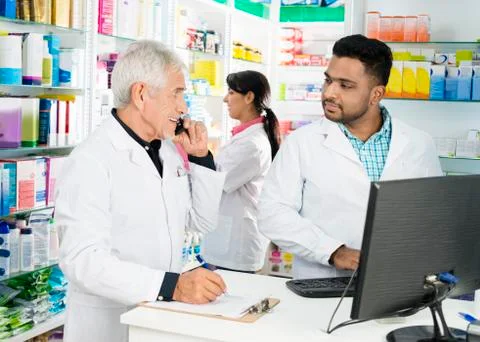 Chemist Using Phone While Looking At Colleagues Using Computer Stock Photos
