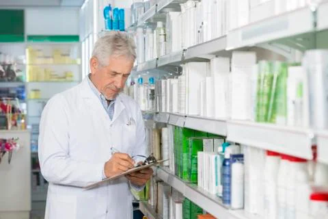 Chemist Writing On Clipboard While Standing By Shelves 写真素材
