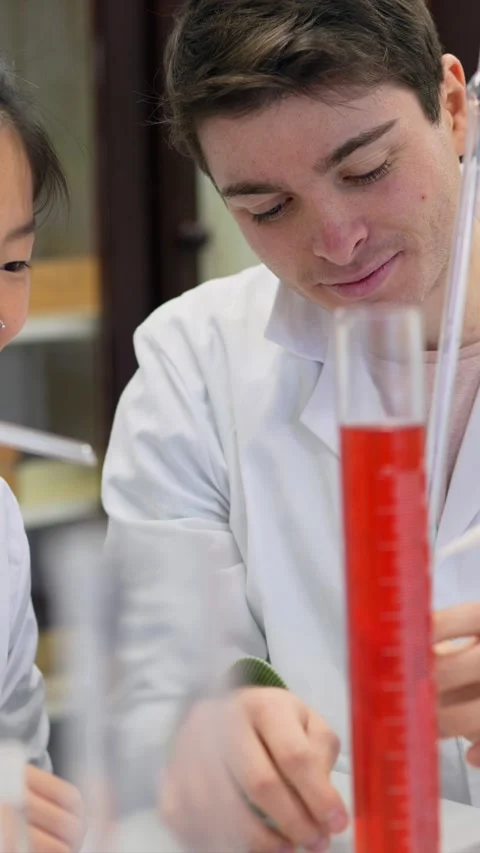 Chemistry students collaborating on experiment with graduated cylinder Stock Footage 302819059