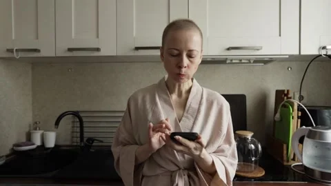 Chemo patient taps smartphone during breakfast in the kitchen at home Stock Footage 329436113