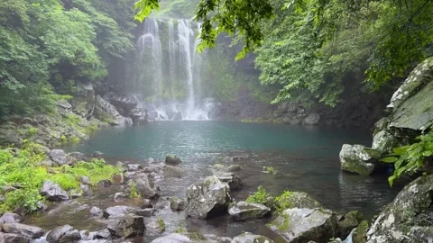 Cheonjeyeon waterfall plunging into a tranquil turquoise pond on jeju island Stockbeeldmateriaal 343065970