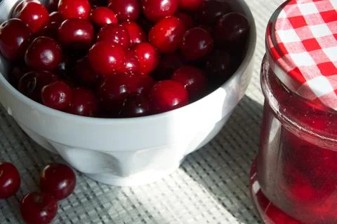 Cherries and a jar of jam on background and fresh fruits on the table, closeup Stock Photos