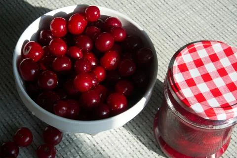 Cherries and a jar of jam on background and fresh fruits on the table, closeup Stock Photos