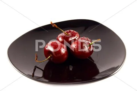 Cherries on a black saucer isolated on white Stock Photos