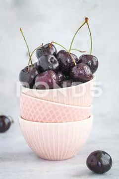 Cherries in three pink bowls stacked on top of each other on a light background Stock Photos