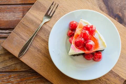 Cherry cheese pie cake in white plate and metal fork on wooden table. Stock Photos