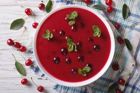 Cherry cream soup with mint in a bowl on a table close-up. Horizontal top vie Stock Photos