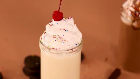 Cherry Dropped Onto Whipped Cream Vanilla Milkshake in Glass Jar Stock Footage 321047024
