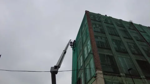 Cherry picker working on warehouse covering building with netting Woolwich Stock Footage 301873612