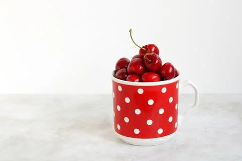 Cherry in a polka dot mug on a light background. Stock Photos