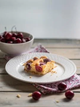 Cherry sponge cake and white bowl of fresh cherries on white wooden table. Stock Photos