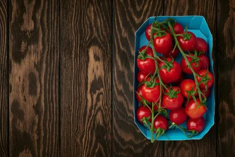Cherry tomato branches in cardboard packing tray on wooden background Stock Photos