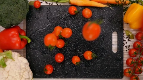 Cherry tomato falling on chopping board framed by fresh vegetables Video stock 104463968