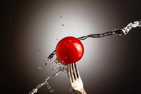 Cherry tomato on a silver fork, jet of water, spray Stock Photos