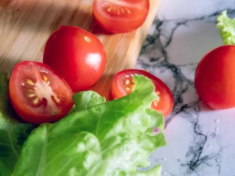 Cherry tomatoes and lettuce leaf on cutting board on marble countertop Stock Photos