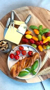 Cherry tomatoes ,cheese slice, basil leaves, flaky twist pastry on wooden board Foto stock