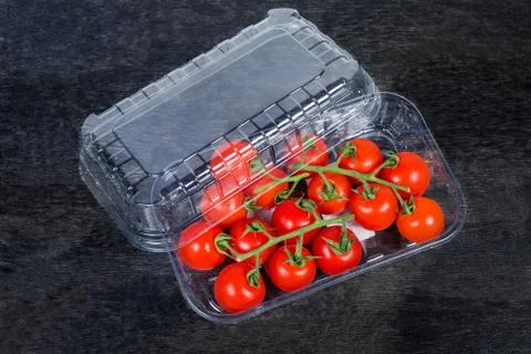 Cherry tomatoes clusters in partly open packaging on black surface Stock Photos