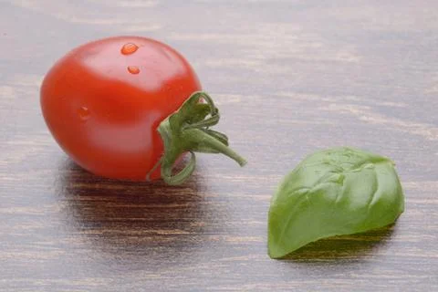 Cherry tomatoes on a dark table. A bunch in drops of water. Basil leaf. Stock Photos
