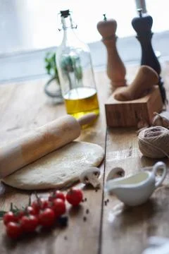 Cherry tomatoes, dough, rolling-pin, olive oil, mortar and pestle lying on ta Stock Photos