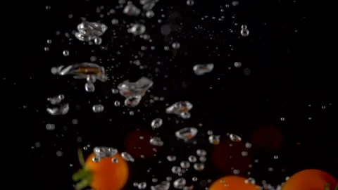Cherry tomatoes falling into clear water with big splash on black background. 스톡 동영상 150566964