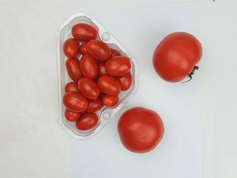 Cherry tomatoes in plastic container and whole tomatoes on white background Stock Photos