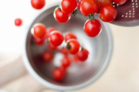 Cherry Tomatoes Tumbling from Metal Colander into Metal Pan 库存照片