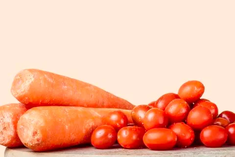 Cherry tomatoes on a wood next to three carrots. Stock Photos