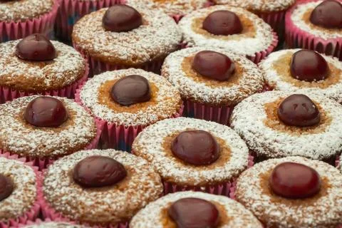 Cherry topped mini cupcakes with powdered sugar on festive bakery display c.. Stock Photos