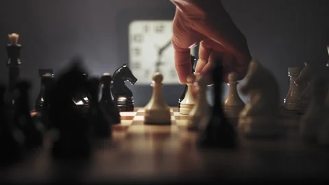 Chess game on brown board in dark environment with clock in background Stock Footage 312822403