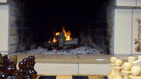 Chess pieces stand on a chessboard in front of the fireplace. Vídeos de archivo 119751091
