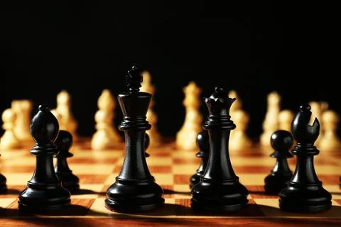 Chess pieces on wooden board against dark background. Competition concept Stock Photos
